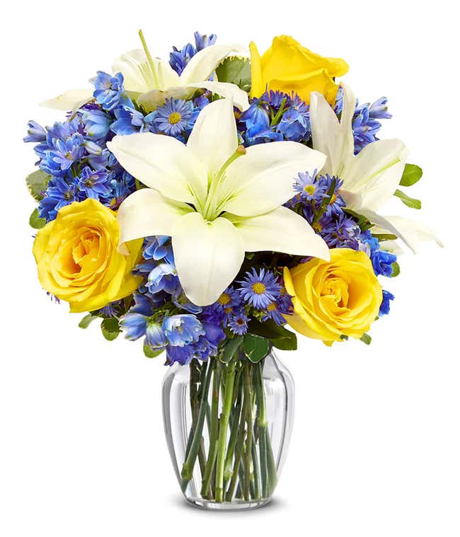 An elegant floral arrangement featuring white Asiatic lilies, yellow roses, blue delphinium, and purple Monte Casino, optionally arranged in a glass vase. This vibrant mix offers a stunning and colorful display.