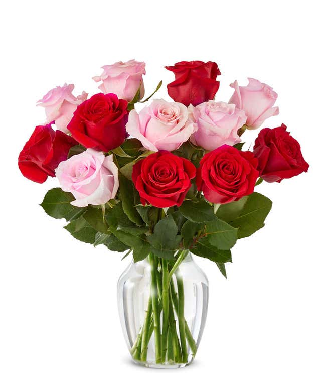 A bouquet of red and pink roses with lush greenery arranged in a clear glass vase.