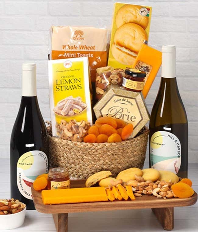 A two-toned woven basket filled with two cheeses, lemon flavored baked goods, crackers, dried apricots, gourmet nuts, and honey, paired with two bottles of wine - Chardonnay &amp; Pinot Noir
