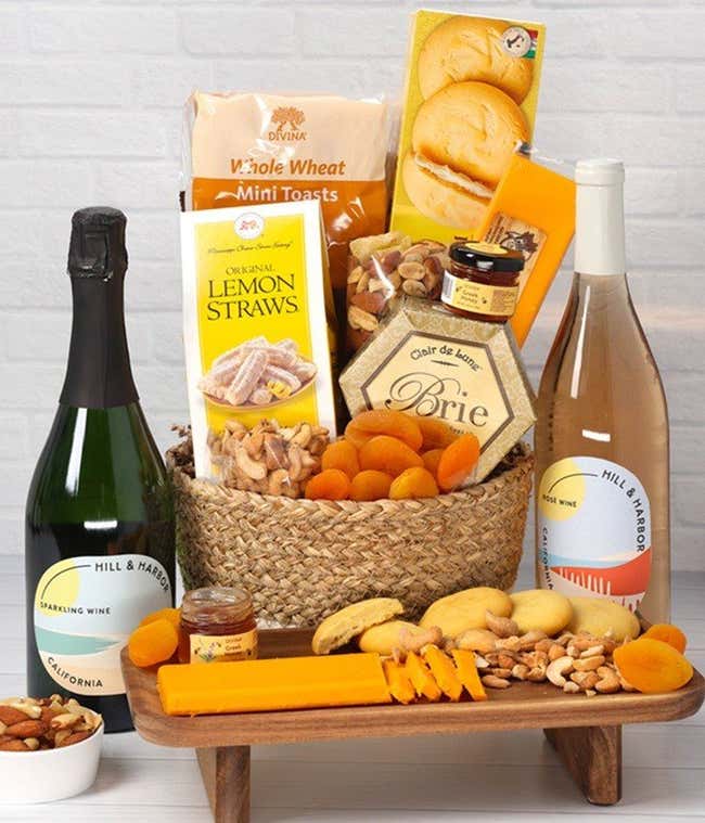 A two-toned woven basket filled with two cheeses, lemon flavored baked goods, crackers, dried apricots, gourmet nuts, and honey, paired with two bottles of wine - Sparkling &amp; Ros&eacute;.
