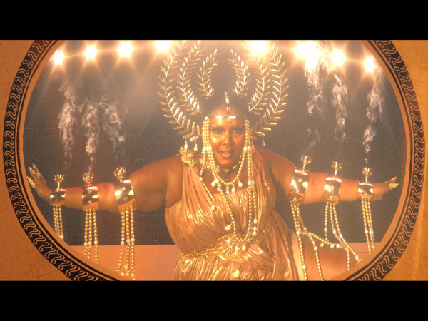 screenshot from Lizzo Rumors music video showing Lizzo with glowy skin golden dress headpiece and arm pieces