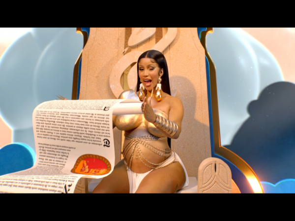 screenshot from rumors music video of cardi b holding scroll while wearing a gold breastplate and teardrop earrings