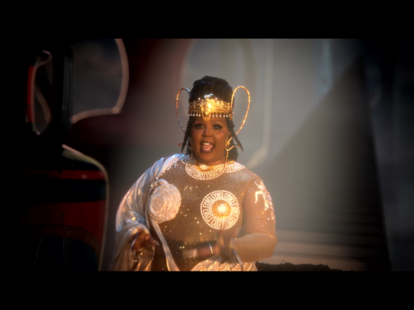 screenshot from rumors music video of lizzo singing in a bedazzled mesh gown long braided hairstyle with golden...